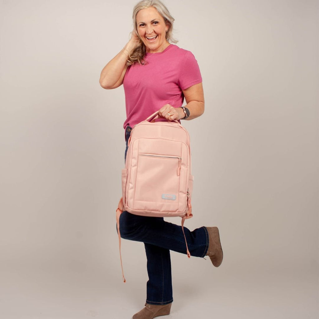 Go-Be Backpack Pink with Floral Interior - stylish and functional travel bag for women. Lightweight and easy to carry with top handle. Woman with pink tshirt holding pink backpack by top handle up to waist.